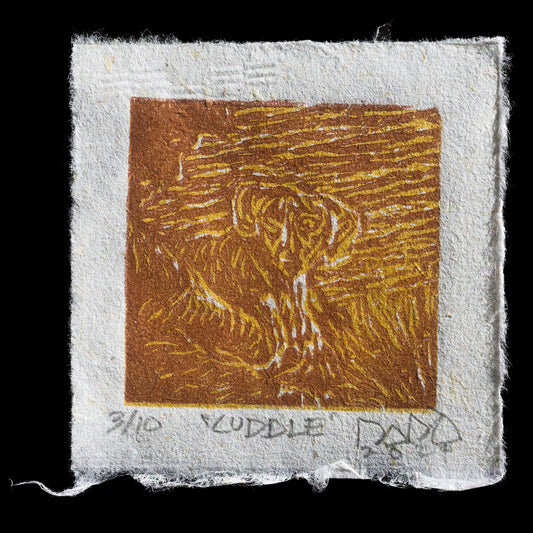 This linocut print, titled 'Cuddle' by Boboy Dado, features a warm brown square with an abstract design at its center. The square is surrounded by a light gray border, creating a sense of depth and contrast. The overall effect is one of cozy warmth and invitation.