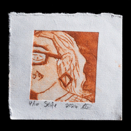 This print, titled 'Selfie', is a work by Louise Wiseman, employing the innovative technique of TetraPak. The print features a close-up view of a woman's face in profile, with her hair flowing down to the right. Her skin tone is depicted in shades of light orange, while her lips are accentuated in a darker orange hue. The background is a subtle blend of grey and white tones.