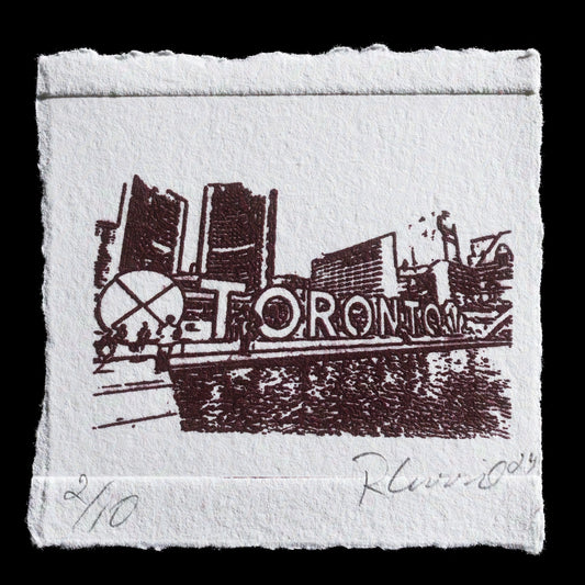 This print, "Nathan Phillips Square" by Robert Currie, showcases a black-and-white image of Toronto's iconic Nathan Phillips Square. The scene depicts the square with its fountain, surrounded by buildings in the background. The print is rendered using intaglio techniques and features laser-cut details.