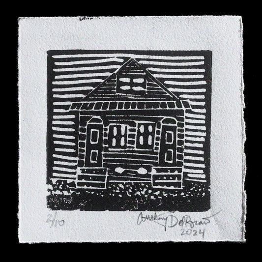 This linocut print, "New Orleans Double Shotgun" by Anthony DelRosario, features a black-and-white composition that showcases a double shotgun house with a pitched roof. The artist's use of relief printing techniques creates a textured surface, adding depth to the image. The print is signed and dated in pencil at the bottom, providing context for its creation.