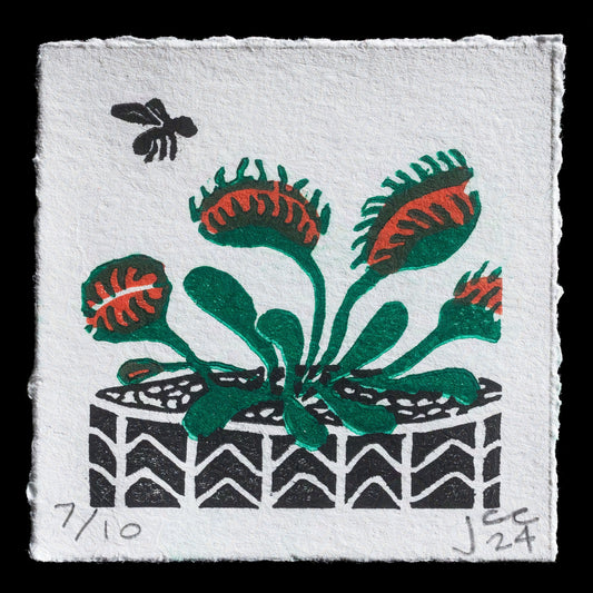 This linocut print features a stylized arrangement of four flowers in shades of green and red, set against a white background with subtle texture. A small bee is depicted flying above the flowers to the left side of the composition. The artist's signature is discreetly placed at the bottom center of the image.