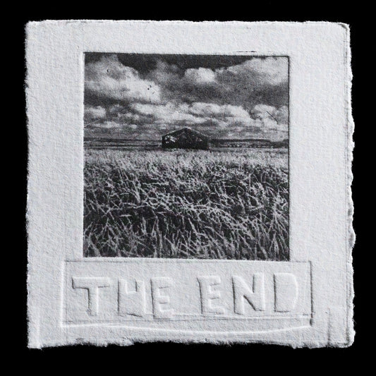 This etching by Pauline Ferrick-Squibb presents a serene black-and-white landscape with a grassy foreground, a small barn under a cloudy sky in the background. The title 'THE END' is discreetly embossed below the image, adding a subtle layer of meaning to this contemplative scene.