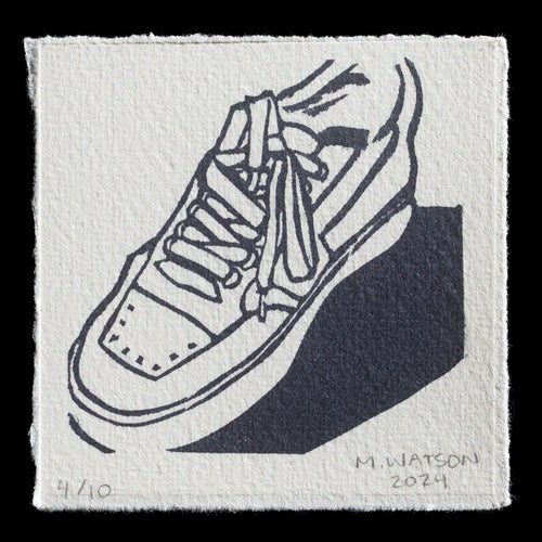 This monochromatic linocut print showcases a shoe in profile view. The black ink highlights white shoe laces against a light gray background, creating a striking contrast. The artist's signature, 'M. Watson,' is discreetly placed at the bottom right corner of the image. The print is signed and dated '2024' in pencil at the bottom left corner.