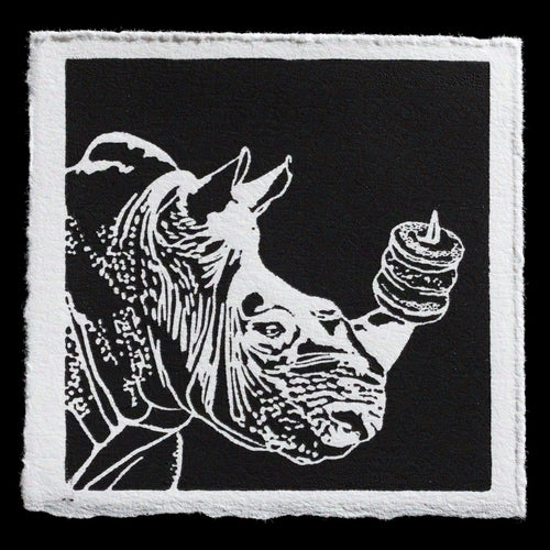 The image depicts a black-and-white woodcut print featuring a rhinoceros holding a stack of donuts. The artwork showcases Wendy Hauschildt's skill in woodcut printing, with a striking contrast between the white lines and dark background. This unique piece highlights Hauschildt's attention to detail and mastery of her craft.