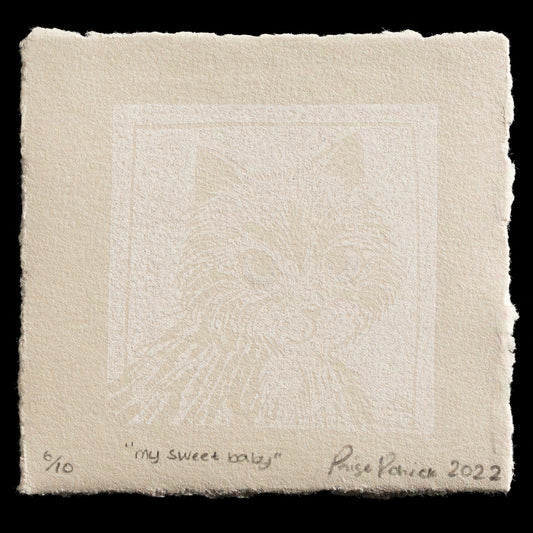 The image depicts a beige square with a subtle white design at its center, featuring two eyes. At the bottom of the square, the words "my sweet baby" are inscribed in black ink.

**Key Details:**

* The square is made of paper or fabric.
* The white design at the center consists of two eyes with eyelashes and eyebrows.
* The text at the bottom reads "my sweet baby".
* The image is signed by Paige Rohrick, 2022.
* The background is black.