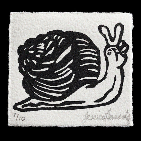 This linocut print, titled "Peace Snail" by Jessica Hernandez, features a stylized snail with its shell in dark gray and the rest of the body in light gray. The snail is depicted facing to the right, conveying a sense of movement and peace.