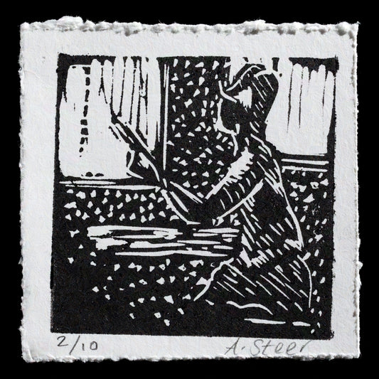 This linocut print, titled "Post race spectator" by Amanda Steer, features a black figure leaning against a wall or fence in front of a window with curtains. The artwork is presented on white paper, showcasing the artist's skillful use of monochromatic tones to evoke a sense of calmness and contemplation.