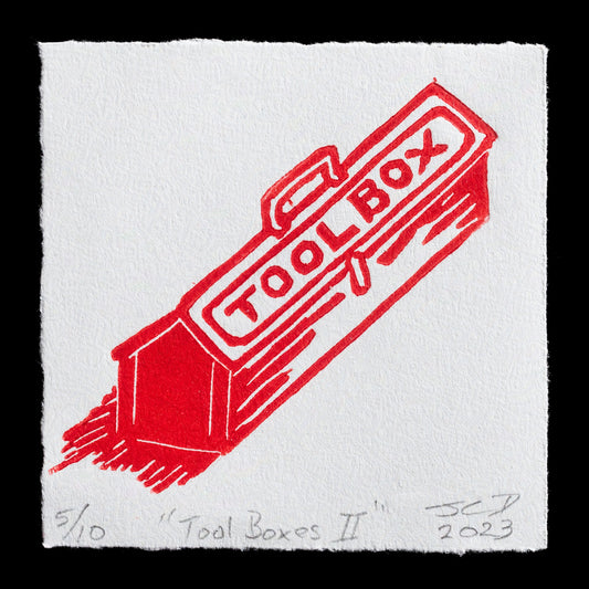 This linocut print depicts a red tool box with the word 'TOOLBOX' printed diagonally across its top. The title "Tool Boxes II" is written in pencil at the bottom left corner, while the artist's signature and year of creation are located at the bottom right corner. The image features a black background, showcasing the print's details in sharp relief.