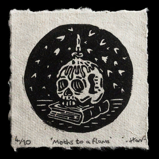 This linocut print by Harvey Douglas-Colgan features a striking black circle with a white skull design at its center. The skull is adorned with a candle flame atop its head, surrounded by scattered moths in the background. The artist's signature and the title "Moths to a flame" are inscribed along the bottom edge of the print.