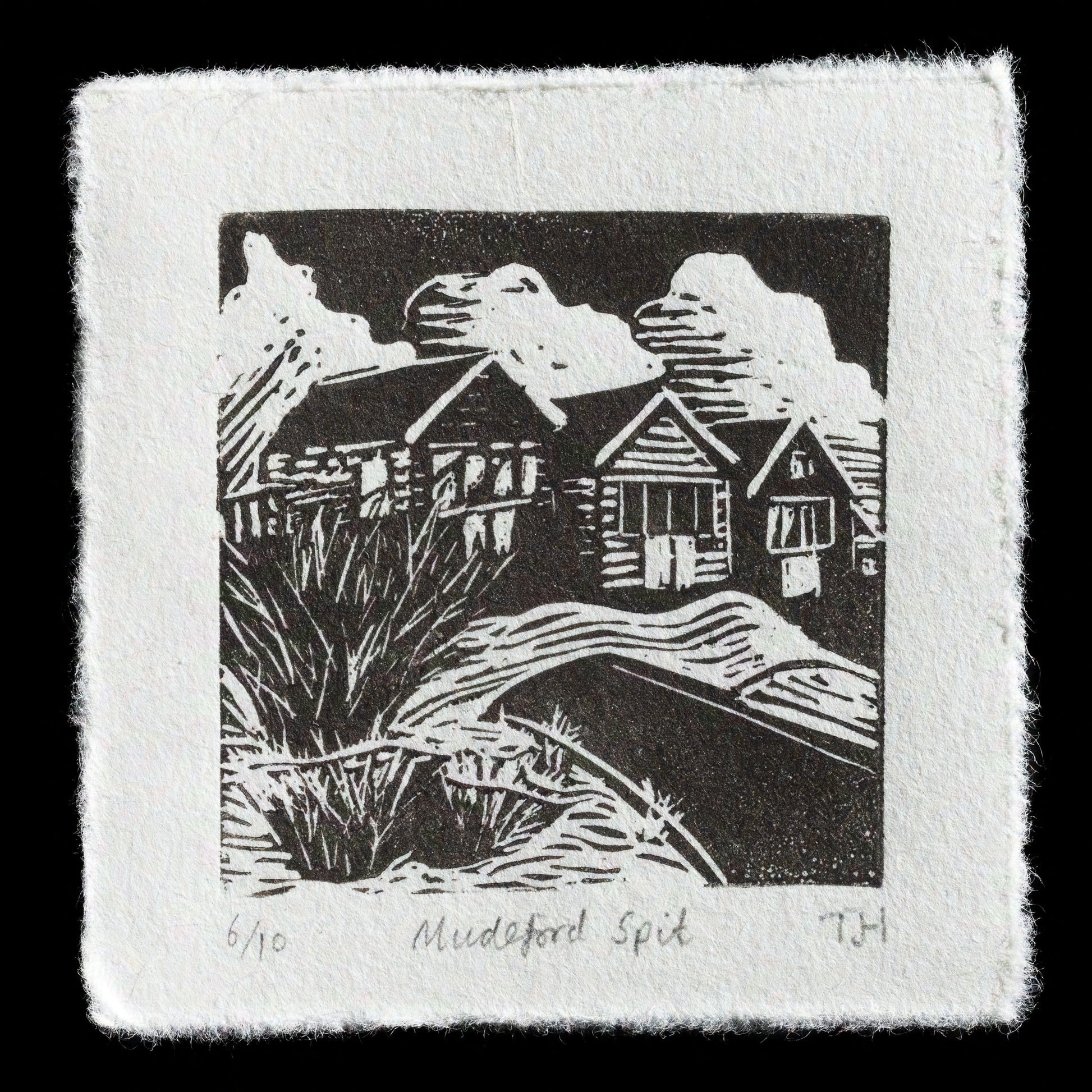 This captivating linocut print, titled "Mudeford Spit" by Tim Holmes, presents a serene coastal scene. The black and white artwork features a tranquil beach with grassy dunes in the foreground, leading to a cluster of small houses on stilts, set against a dramatic dark sky with fluffy clouds. The image is marked with the artist's initials "TH" and numbered "6/10", suggesting it is part of a limited edition series.