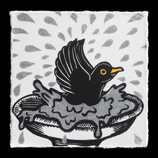 This linocut print titled "Splish-Splash" by Kat Parker features a black bird with yellow accents perched atop an overflowing bowl or dish, set against a white background with scattered grey raindrops. The artist's use of bold lines and watercolor-style colors creates a playful and whimsical atmosphere.