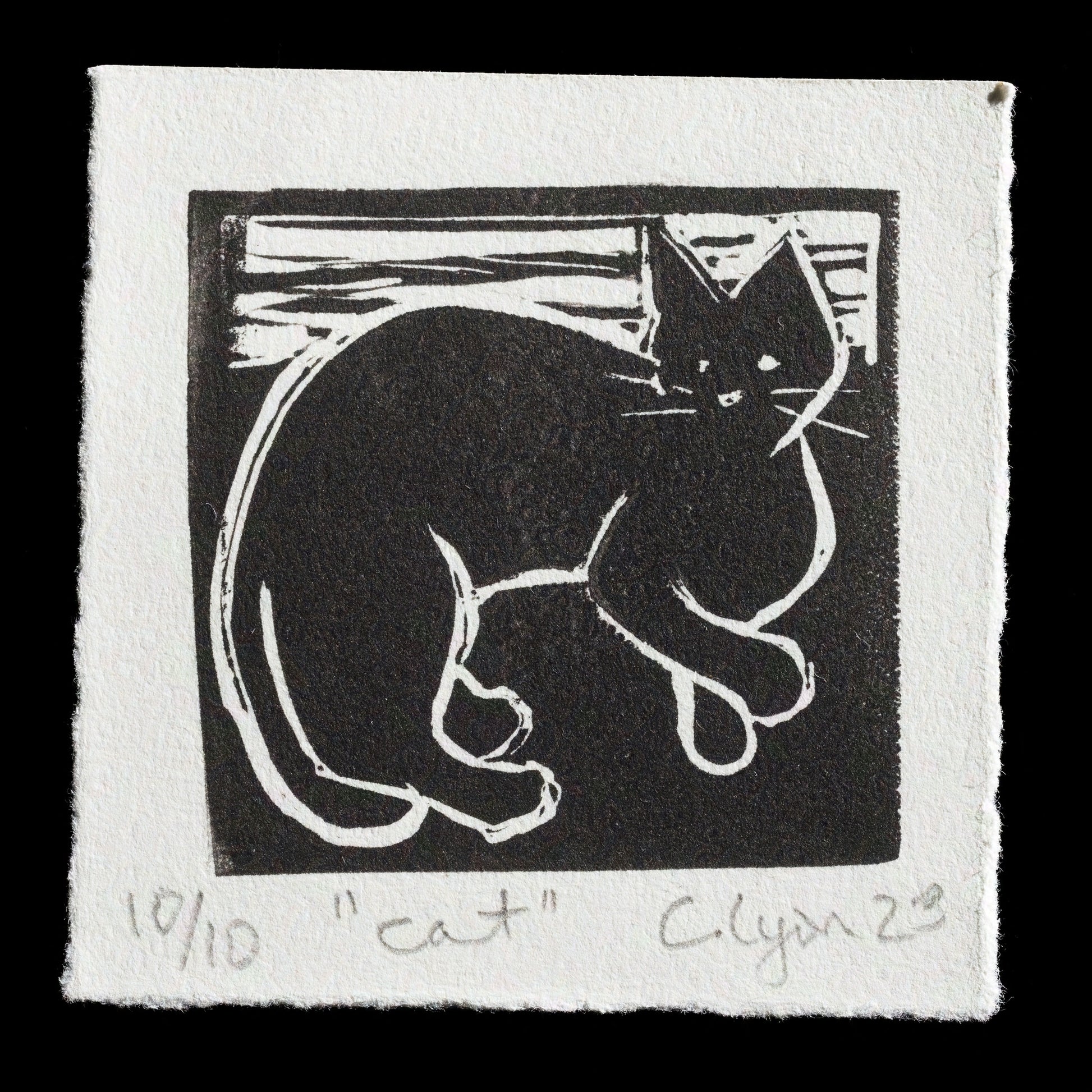 This linocut print, "Cat" by Cristi Lyon, features a black cat with white highlights on a cream-colored background. The artwork showcases the artist's skill in capturing the subject's essence through bold lines and subtle color choices.