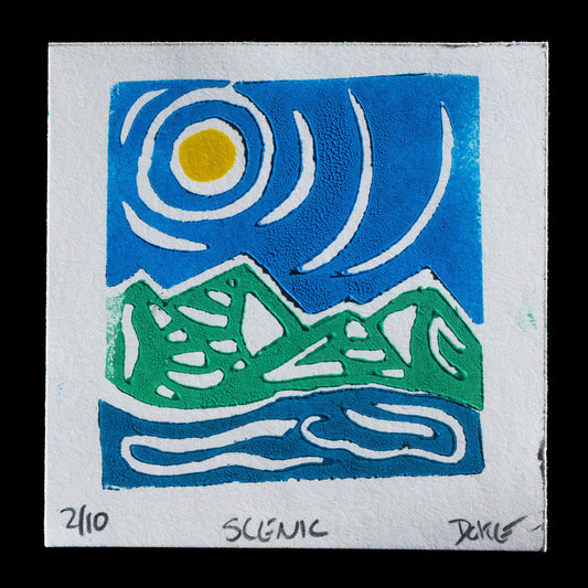 This linocut print, titled "Scenic" by Ashley Doke, features a serene landscape with mountains set against a blue sky. The dominant colors are deep blues and greens, while a bright yellow sun peeks out from behind the mountain range in the top left corner. White accents add subtle highlights to the scene.