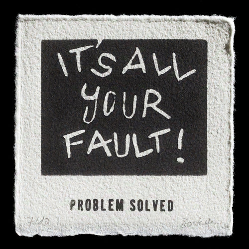 This print by Carla Zockoll features a linocut design with bold black text that reads 'ITS ALL YOUR FAULT', set against a textured off-white background. The phrase is centered within a square frame, creating a striking visual effect.