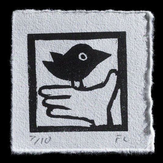 This linocut print features a charming black silhouette of a bird perched on a hand, surrounded by a simple square border with a black outline. The image is rendered in monochromatic tones, comprising only black ink on white paper, creating a striking contrast that highlights the delicate details of the artwork.